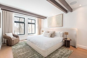 A bedroom with a large bed, a chair, a bedside table, a lamp, and a window with curtains. - Villa Eclipse Solaire | Hot tub & Sauna  | Walk to Ski-in Ski-out | Tremblant Living (Mont-Tremblant)