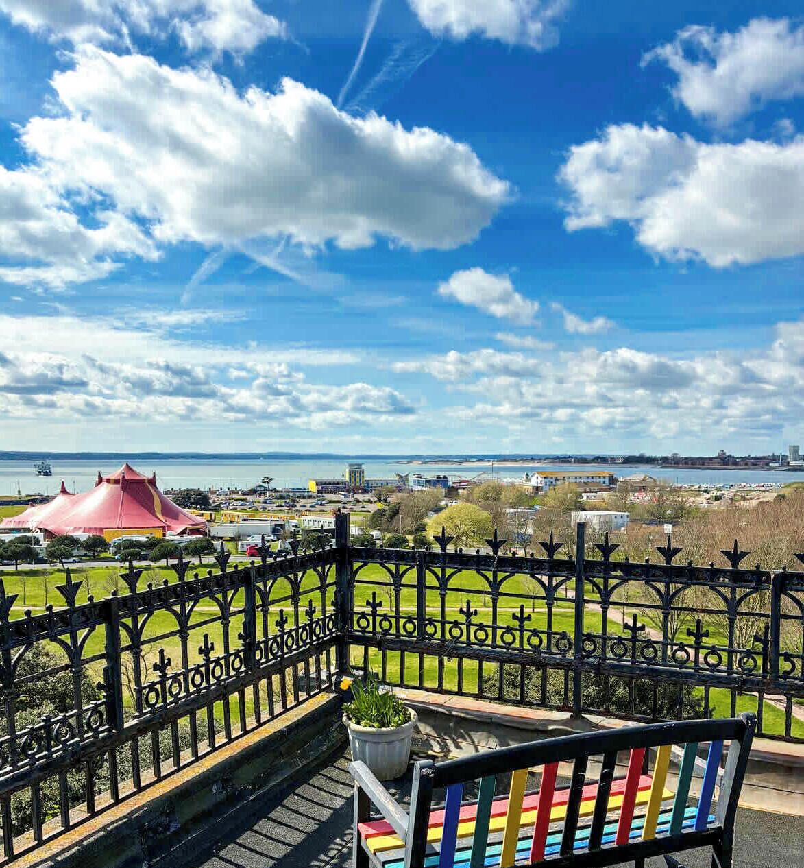 Een balkon met uitzicht op een stadslandschap, een waterpartij en een gebouw met rode daken.