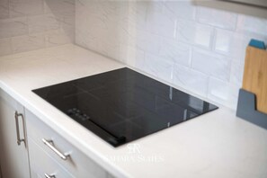 Une cuisine dotée d’une plaque de cuisson à induction noire, de meubles blancs et d’un dosseret en marbre.