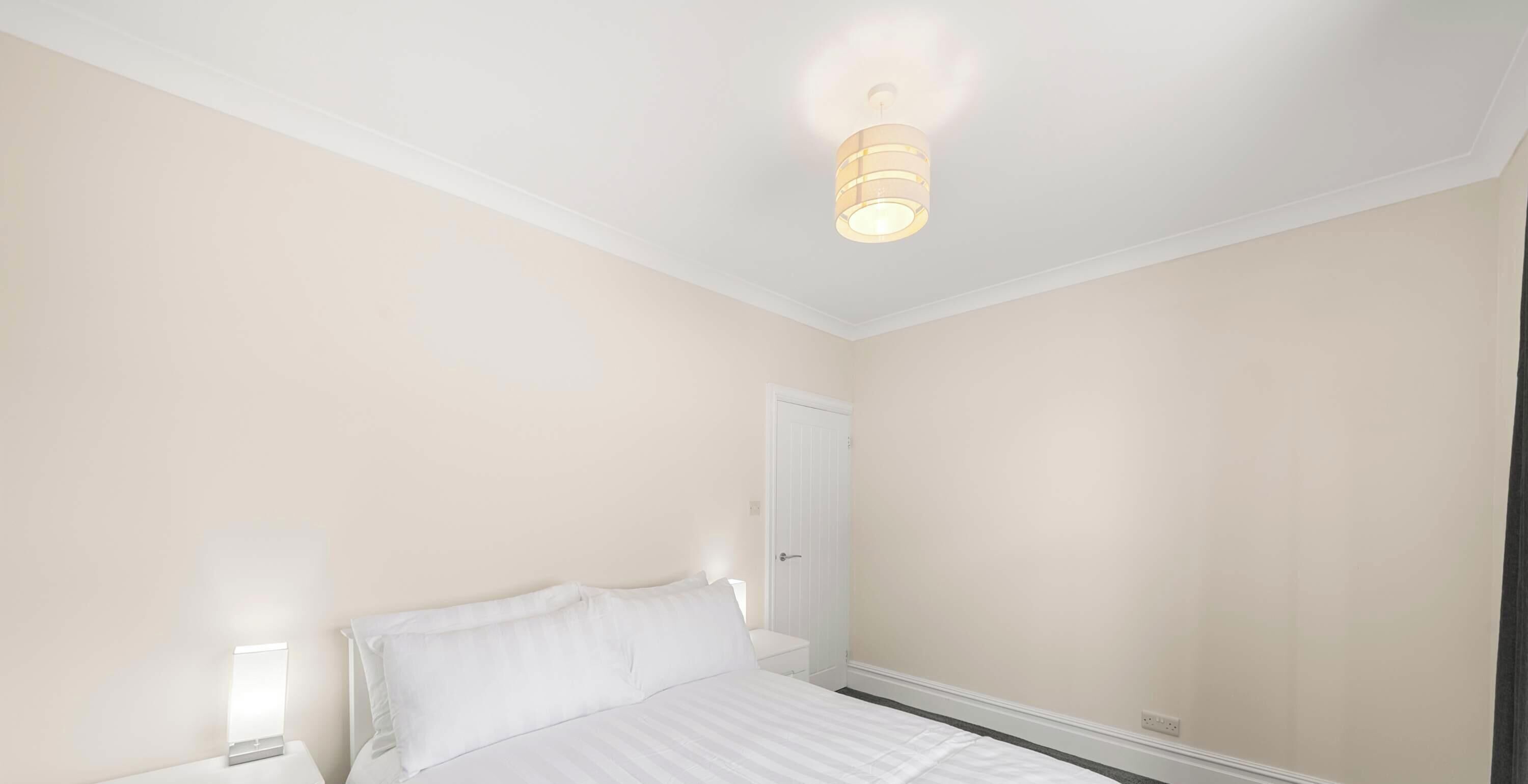A bedroom with a bed, bedside lamps, a door, and a ceiling light fixture.
