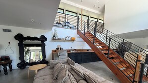 Un interior modern amb un sofà, un mirall gran, una escala i una zona de cuina.
