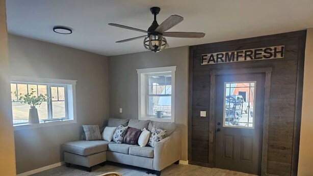 A living room with a sectional sofa, a ceiling fan, and a door labeled 'FARMFRESH'.