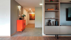 A modern living room with a wooden floor, a red accent wall, a bookshelf, and a flat-screen TV. - Polanco Family Terrace By The Local Way (Mexico City)