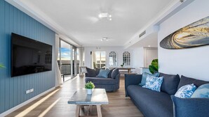 Ein modernes Wohnzimmer mit großem Flachbildfernseher, einer Couch, einem Couchtisch und einem großen Fenster.