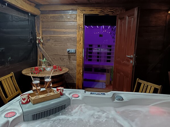 A wooden cabin interior with a hot tub, a table with candles, and a view through a door.