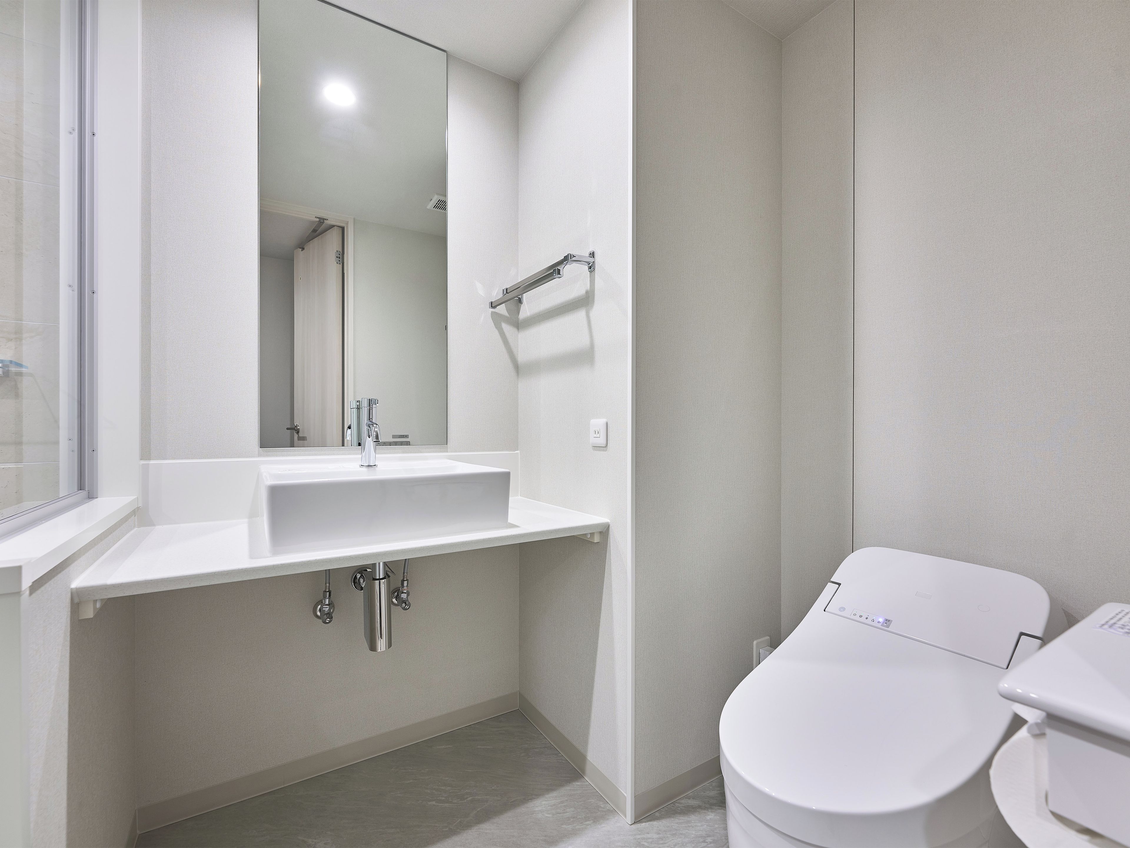 Un baño moderno con lavamanos, espejo y retrete blancos.