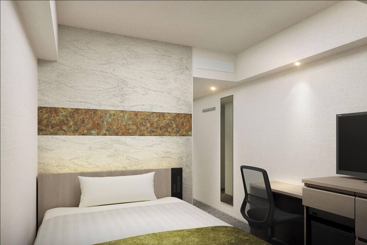 A hotel room with a bed, a desk, a chair, a television, and a patterned wall.