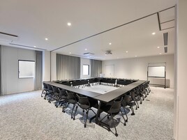 Un salón de conferencias con una larga mesa, sillas, una pizarra y un proyector.