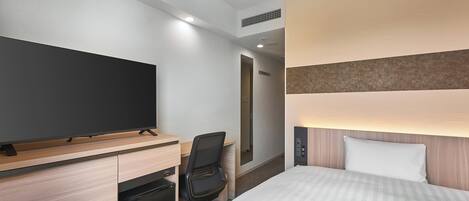 A hotel room with a bed, a desk with a flat-screen TV, a chair, and a mini-fridge.