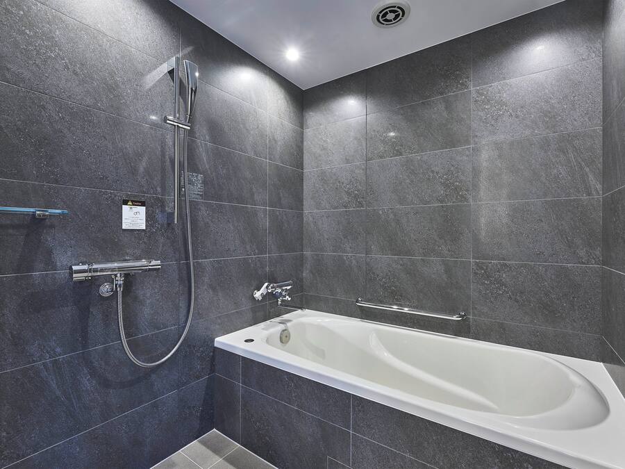 A modern bathroom with a bathtub, shower, and handrails.