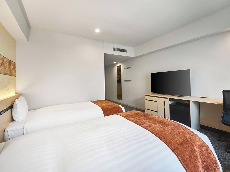 Ein Hotelzimmer mit zwei Betten, einem Schreibtisch, einem Flachbildfernseher und einem begehbaren Kleiderschrank.