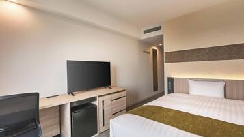 Une chambre d’hôtel comprenant un lit, un bureau avec une télévision, une chaise, un petit réfrigérateur et une table de chevet.