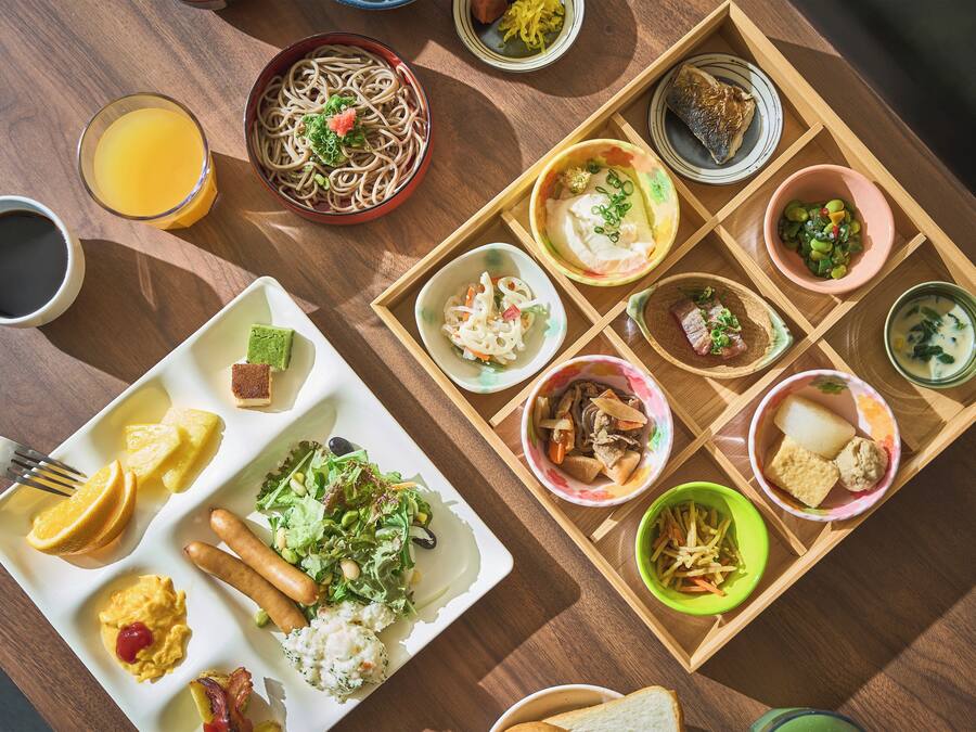 A variety of dishes arranged on a wooden tray, including noodles, salad, and different types of soup.