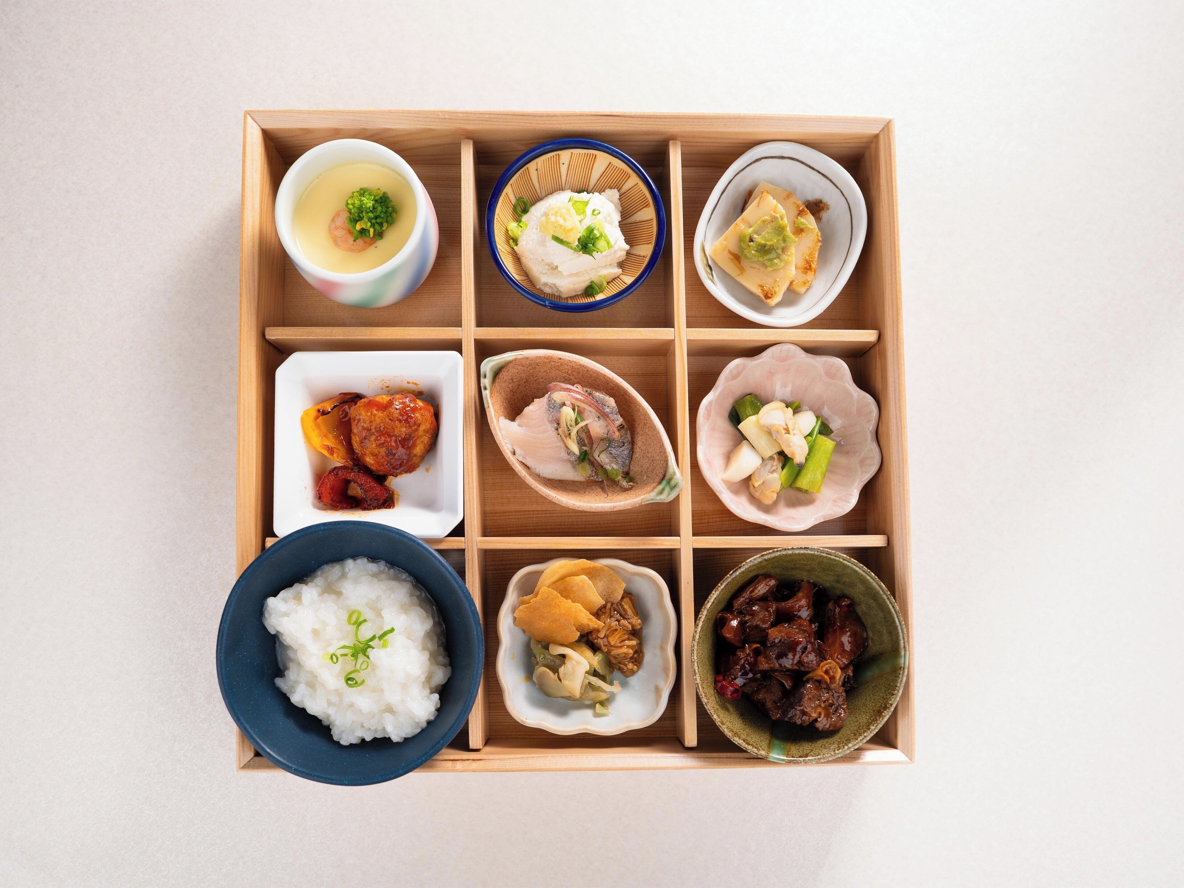 A wooden tray with various Japanese dishes, including rice, soup, and meat dishes.