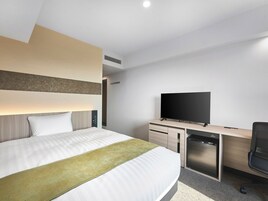 Habitación de hotel moderna con una cama grande, un televisor de pantalla plana, un escritorio con computadora y un lavavajillas compacto.