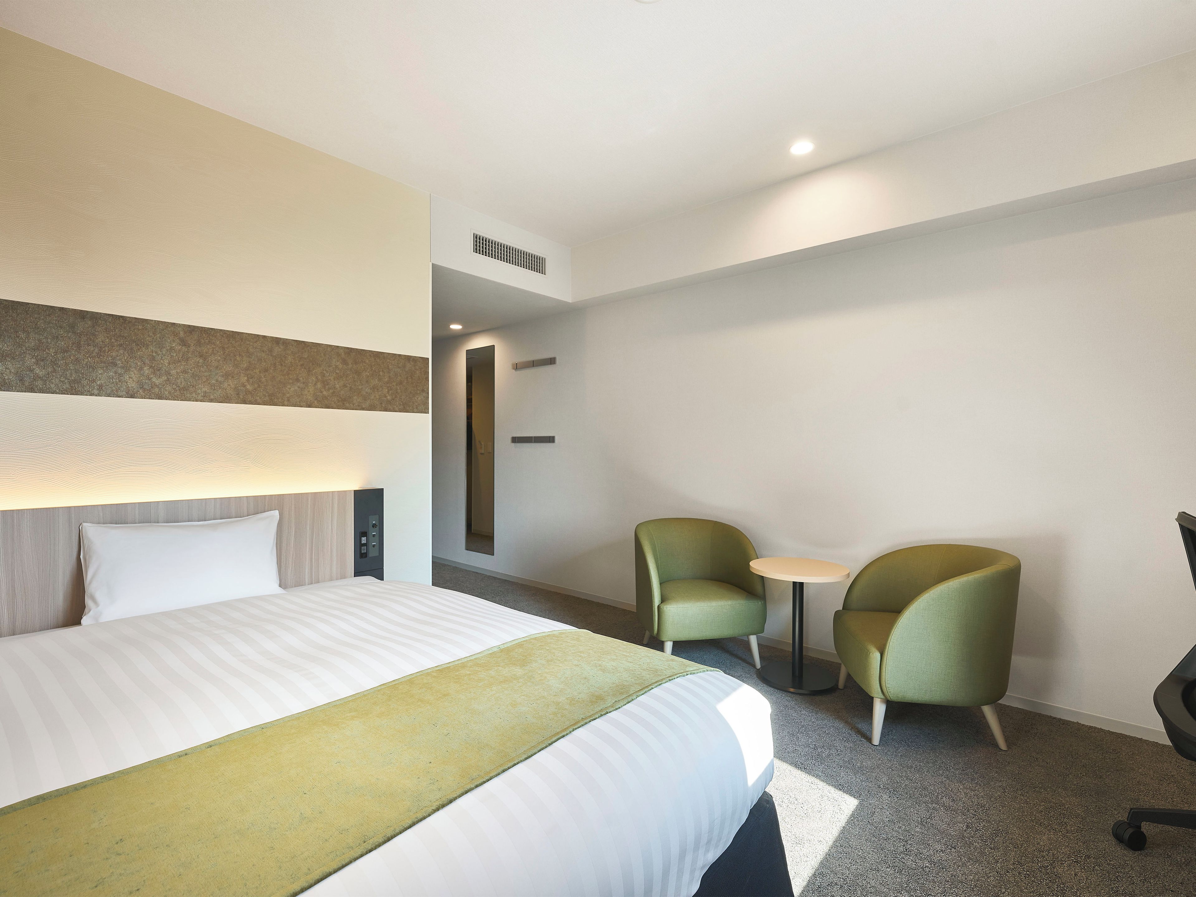 A hotel room with a bed, two chairs, a small table, and a mirror.