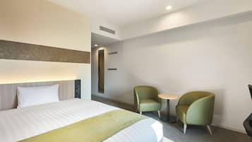 Quarto de hotel com uma cama, duas cadeiras, uma mesinha e um espelho.