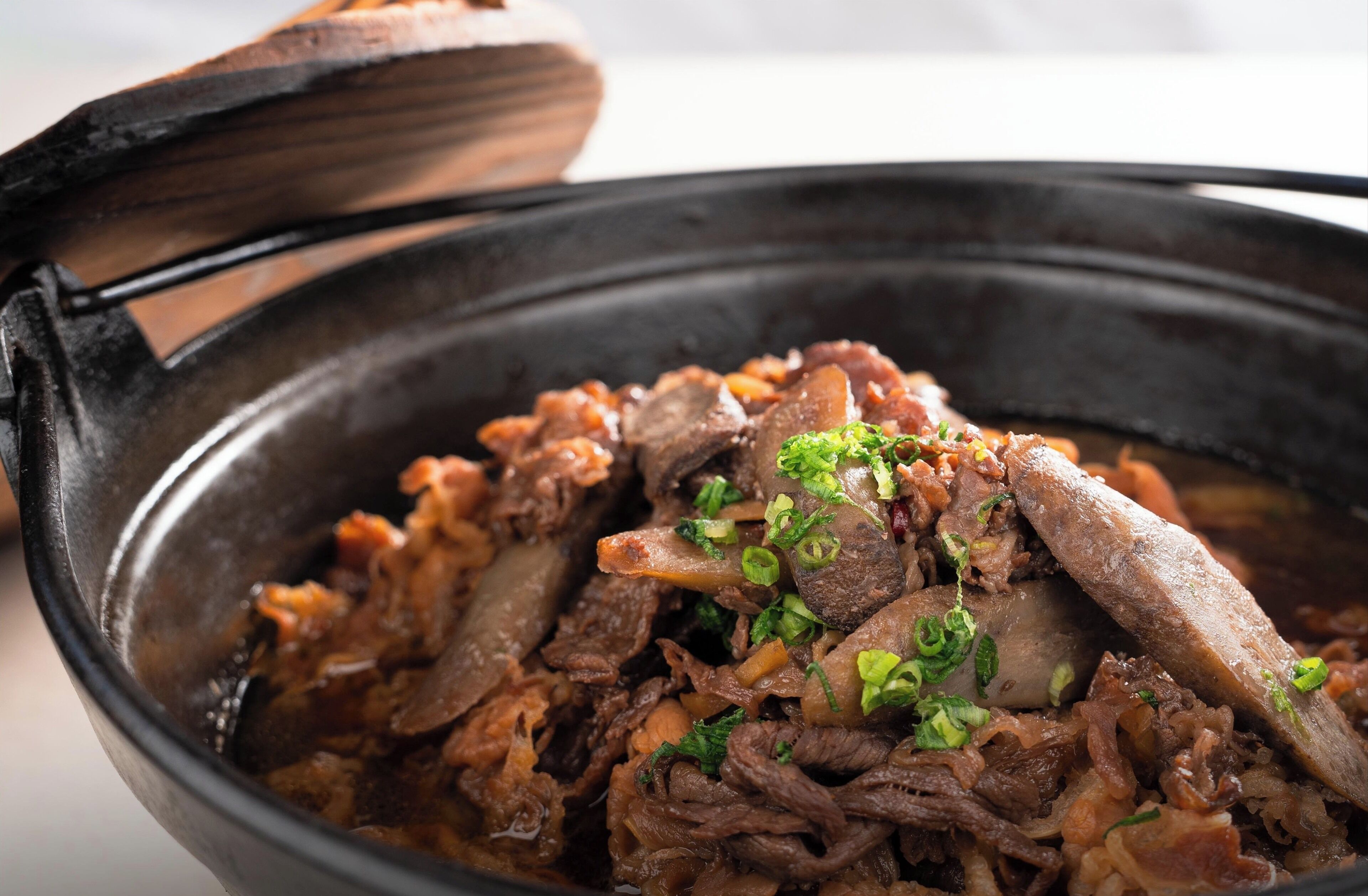 A close-up of a dish with meat and vegetables in a black bowl.