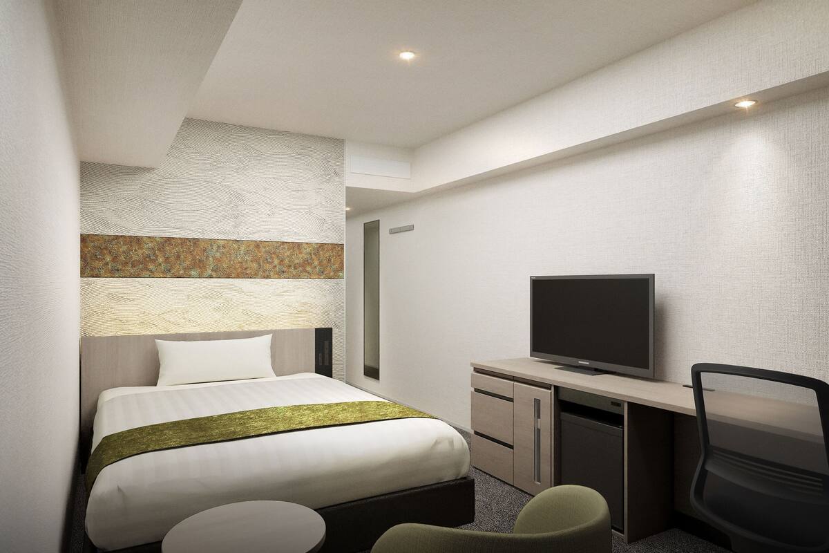 A modern hotel room with a bed, a TV, a desk, and a chair.