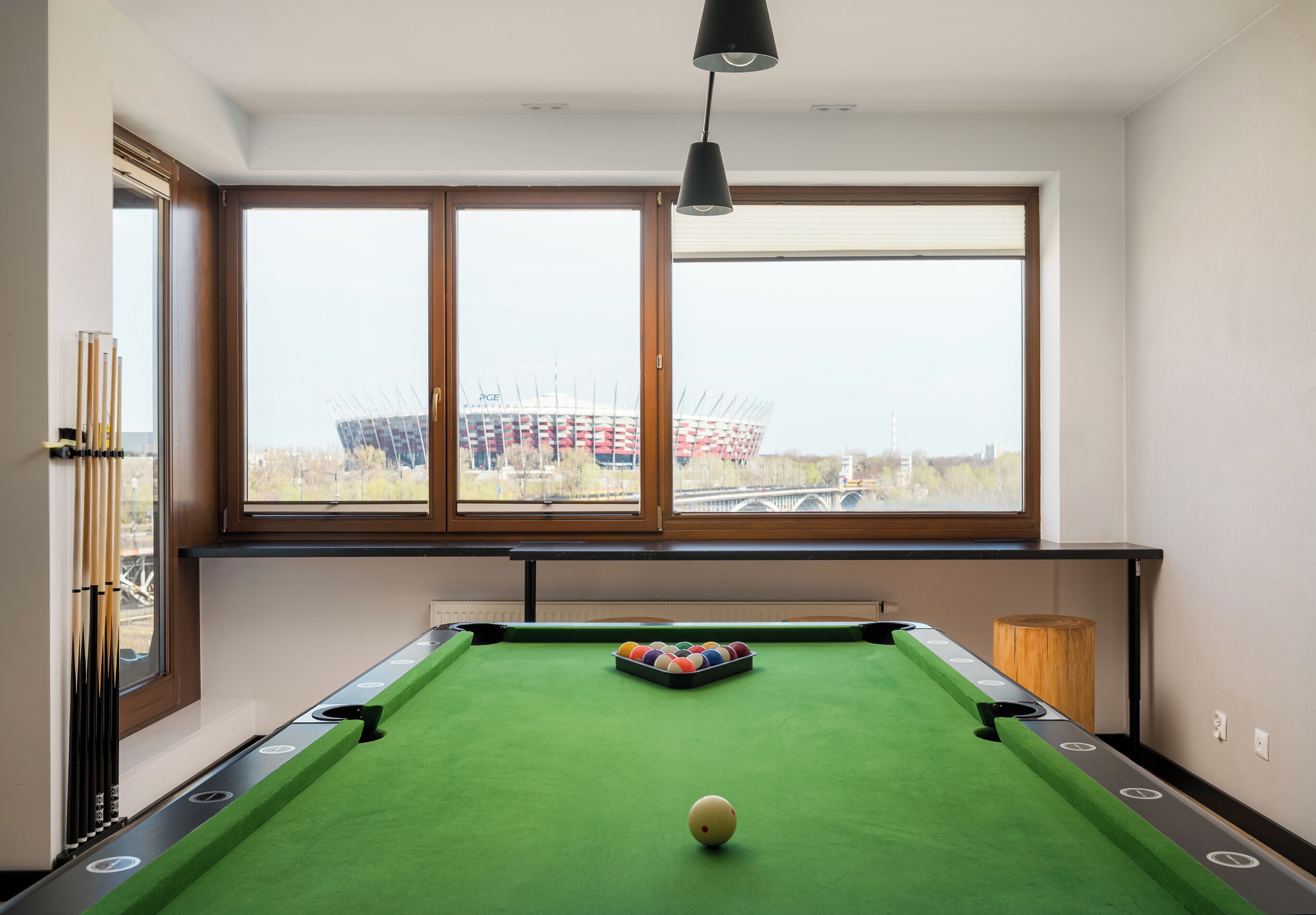 Une table de billard avec des billes, une fenêtre donnant sur un pont et une lampe.