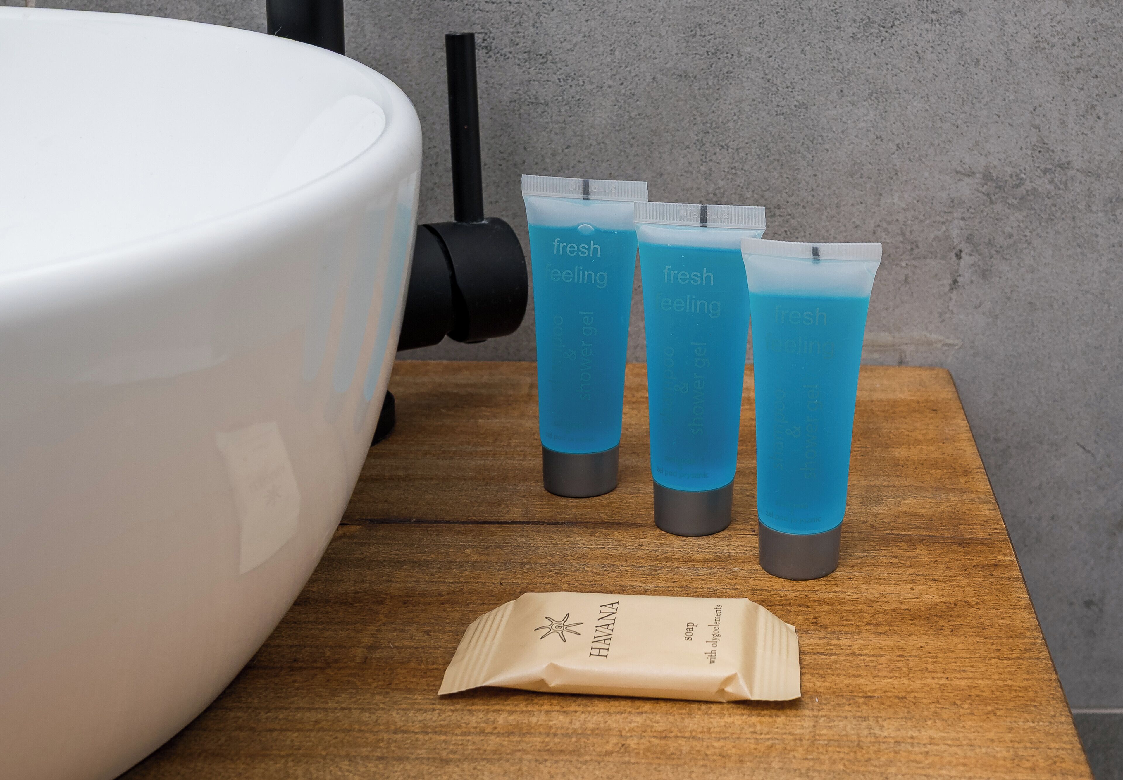 A bathroom with a white bathtub, three blue soap dispensers, and a soap bar labeled 'HAVANA'.