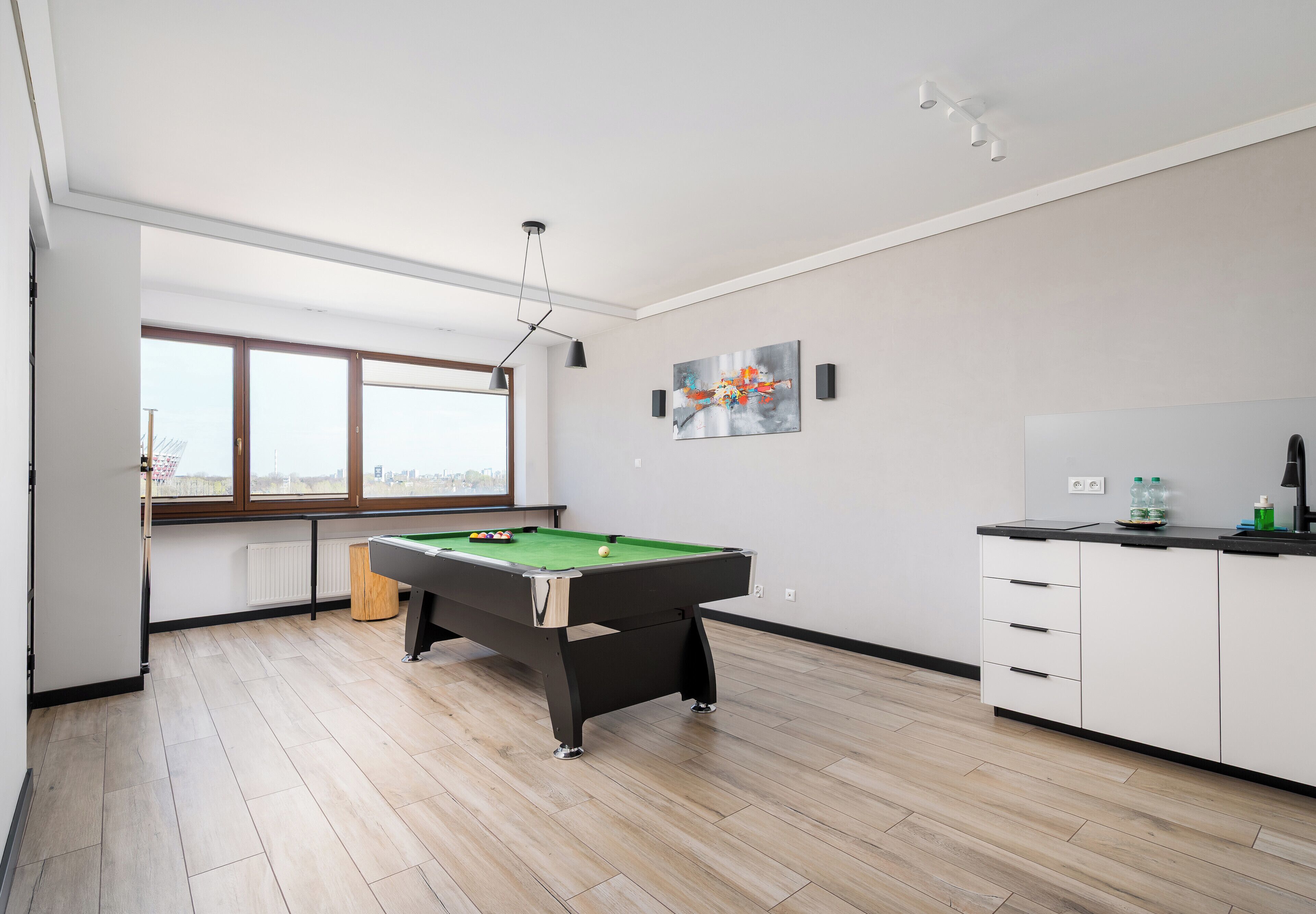 A modern room with a pool table, a window with a view, and a cabinet with bottles.