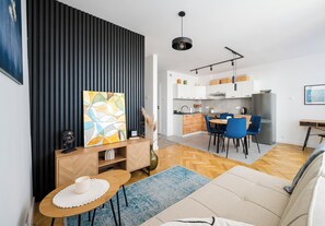 A modern living room with a sofa, a dining table, and a kitchen in the background. - Krasiński Garden Skyline Apartment (Warszawa)
