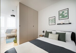 A bedroom with a bed, bedside table, lamp, and wall art. - Krasiński Garden Skyline Apartment (Warszawa)