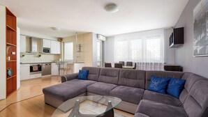 Een moderne woonkamer met een modulaire bank, een glazen salontafel en een keuken op de achtergrond.