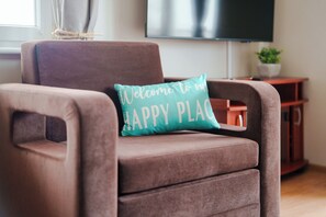 Een bruine fauteuil met een blauwgroen kussen waarop staat 'Welkom in ons HAPPY PLACE'.