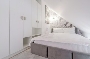 Un dormitorio con cama, armario, radiador e iluminación montada en la pared.