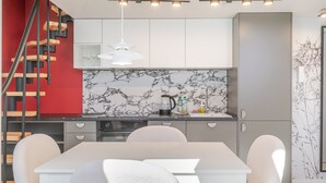 Una cocina moderna con salpicadero de mármol, una mesa de comedor con sillas y una escalera con escalones de madera.