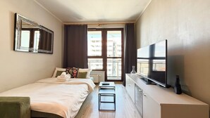 Ett hotellrum med en säng, en tv, ett skrivbord och ett fönster med utsikt över byggnader.