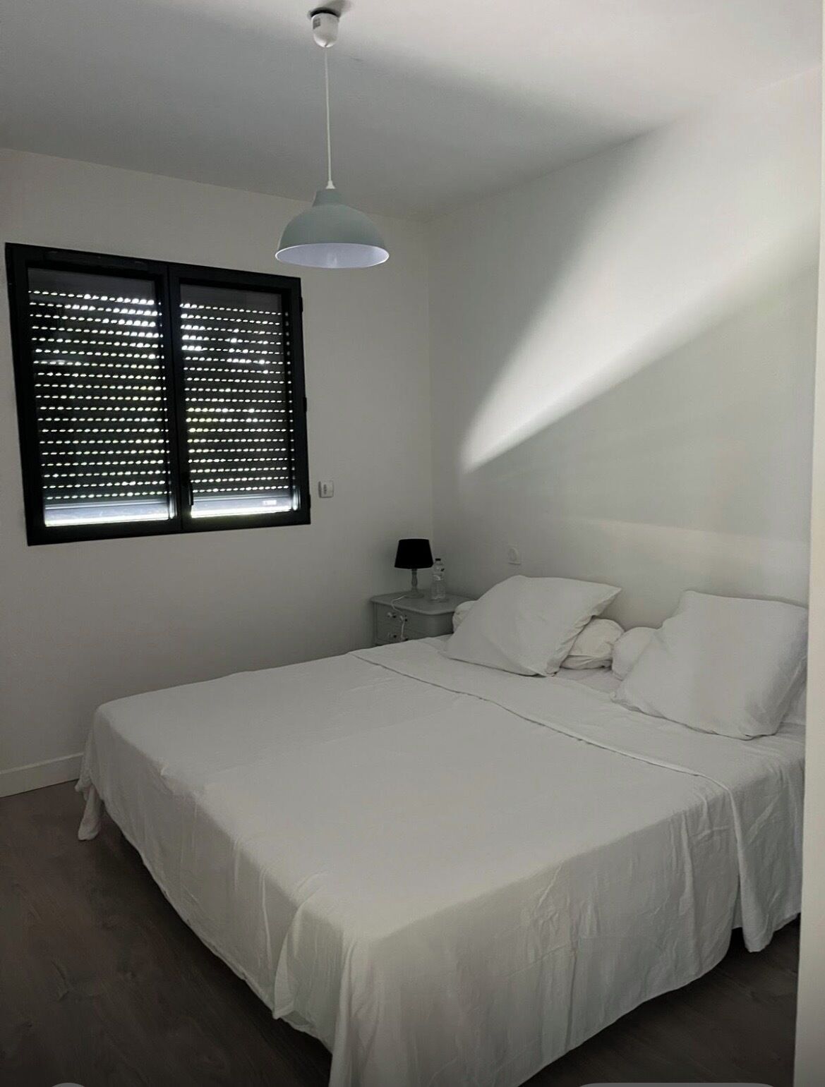 A bedroom with a bed, a nightstand, a lamp, and a window with blinds.