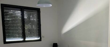 A bedroom with a bed, a nightstand, a lamp, and a window with blinds.