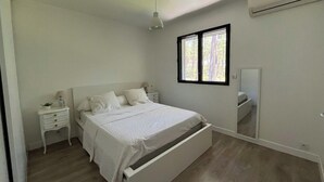 A bedroom with a bed, a nightstand, a lamp, a window, and an air conditioning unit. - Large air-conditioned family home with private, heated, secure swimming pool (Seignosse)