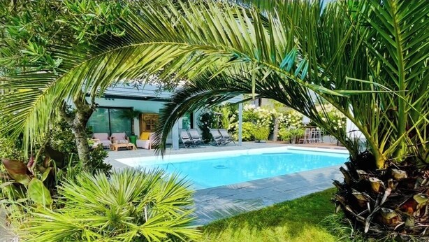 A swimming pool surrounded by lush greenery and a covered seating area. - Large air-conditioned family home with private, heated, secure swimming pool (Seignosse)