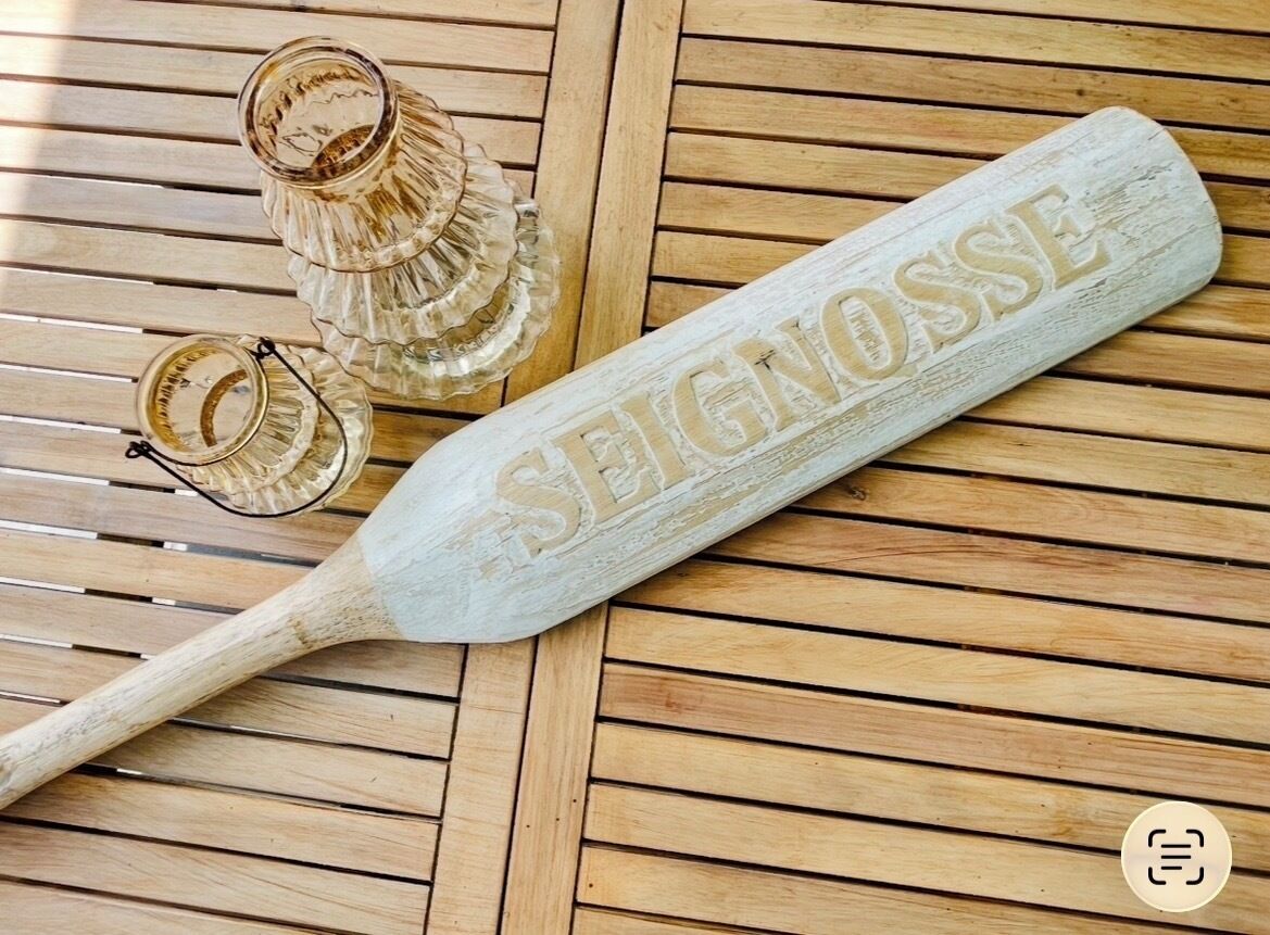 Una taula de fusta amb una placa blanca gravada amb 'SEIGNOSSE' i una paleta de fusta.