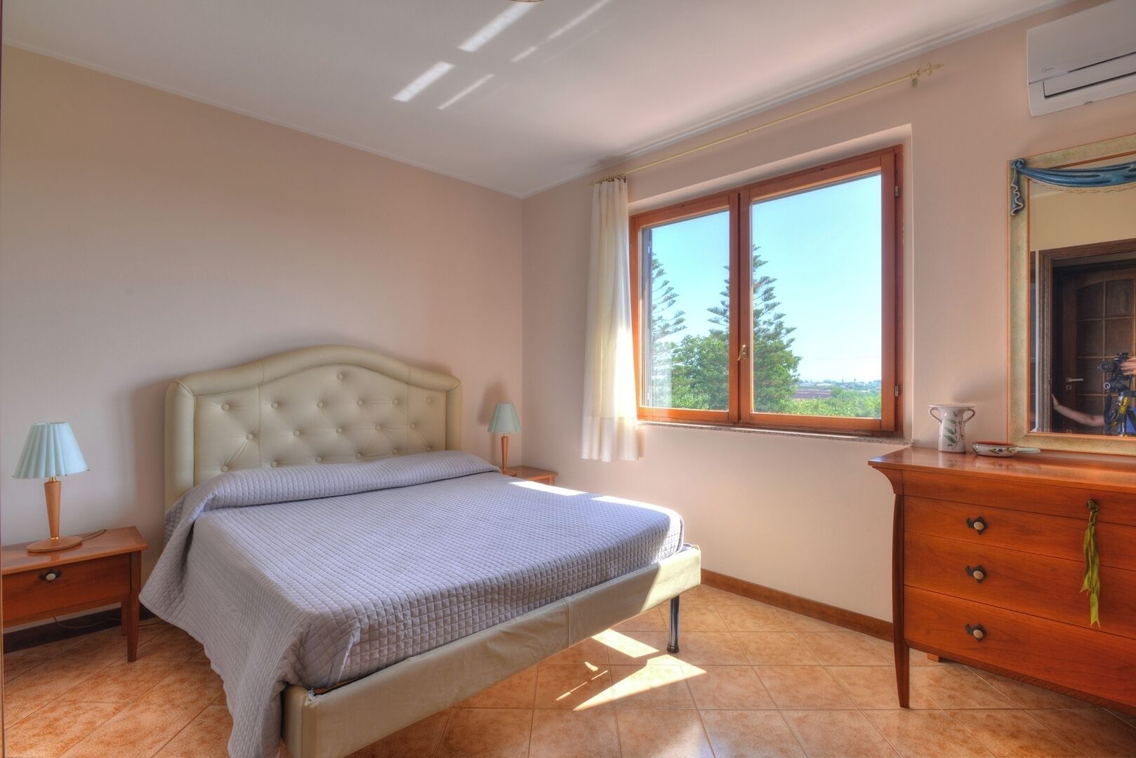 A bedroom with a bed, nightstands, a dresser, a window with a view, and an air conditioning unit.