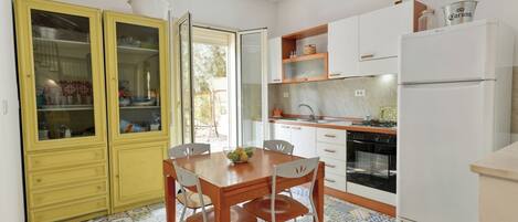 A kitchen with a dining table, chairs, cabinets, a refrigerator, and a window.