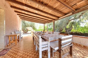Eine überdachte Terrasse mit Esstisch, Bänken und Blick auf Bäume.