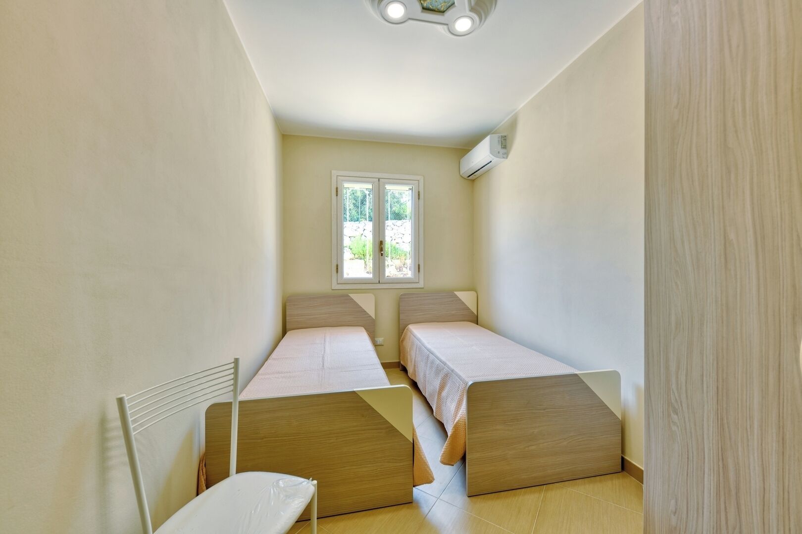 A narrow room with two single beds, a window, and an air conditioning unit.
