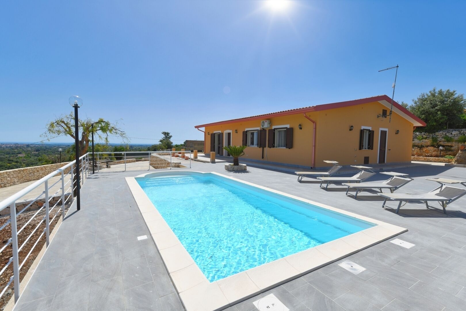 A swimming pool with lounge chairs, a building with a red roof, and a clear sky.