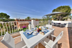 Eine Terrasse mit Frühstückstisch, Sitzmöbeln im Freien und Blick auf die umliegende Landschaft.