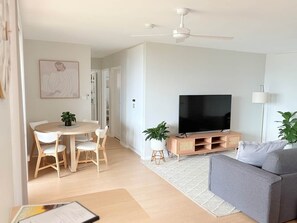 Un salon moderne doté d’un téléviseur à écran plat, d’un canapé gris, d’une table à manger avec des chaises et d’un ventilateur de plafond.