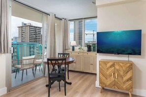 A room with a dining table, chairs, a TV, a cabinet, and a view of buildings through a glass door. - [New] Walk Score 95 | Mtn+City View | Kitchenette (Honolulu)