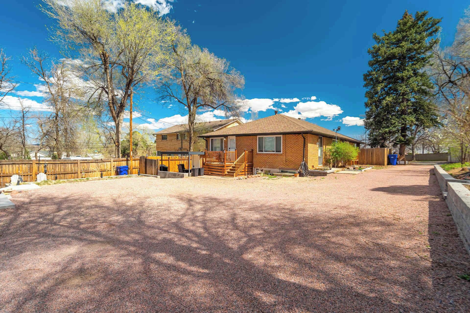 A single-story brick house with a covered porch, a fenced yard, and a gravel driveway.