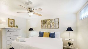 Un dormitorio con cama, mesitas de noche, cómoda, ventilador de techo y una obra de arte en la pared.