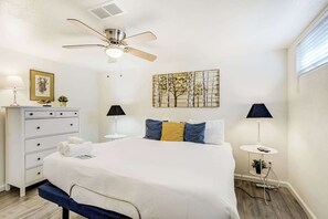 A bedroom with a bed, bedside tables, a dresser, a ceiling fan, and a wall-mounted artwork.