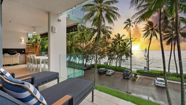 Ein Balkon mit Blick auf den Ozean und Palmen, ein Essbereich mit Stühlen und einem Tisch sowie eine Küche mit modernen Geräten.
